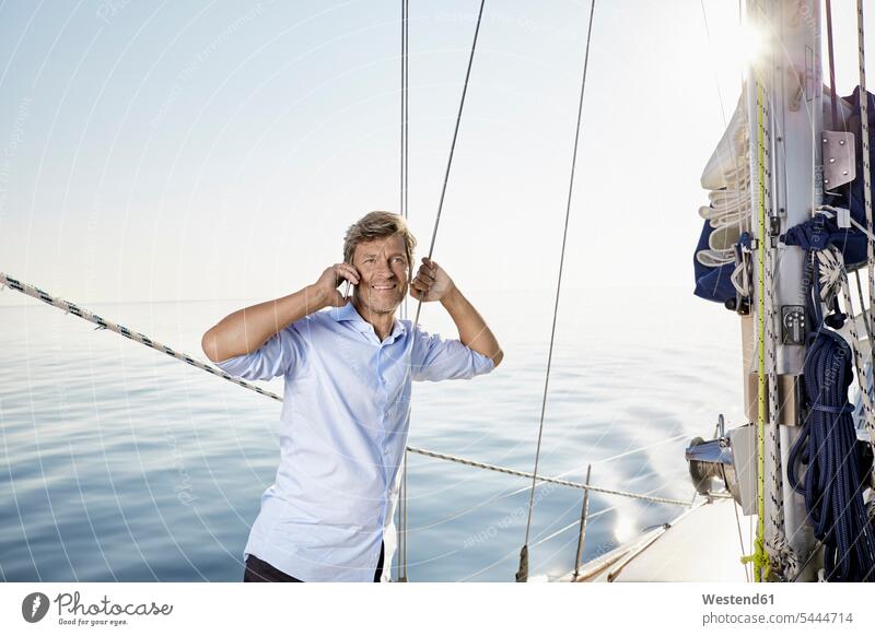 Portrait of smiling mature man lon the phone on his sailing boat portrait portraits men males boat sports Adults grown-ups grownups adult people persons