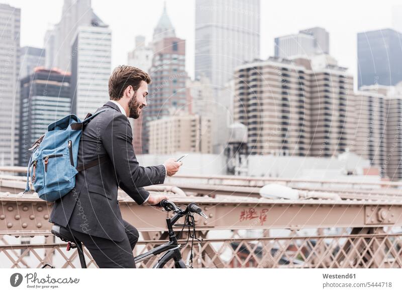 USA, New York City, businessman on bicycle on Brooklyn Bridge using cell phone Businessman Business man Businessmen Business men bridge bridges bikes bicycles