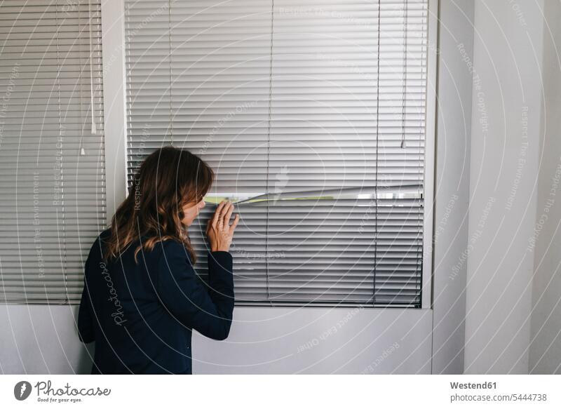 Woman standing by window, spying through blinds roller blind roller blinds Monitoring woman females women watching observing observe secret Secretive
