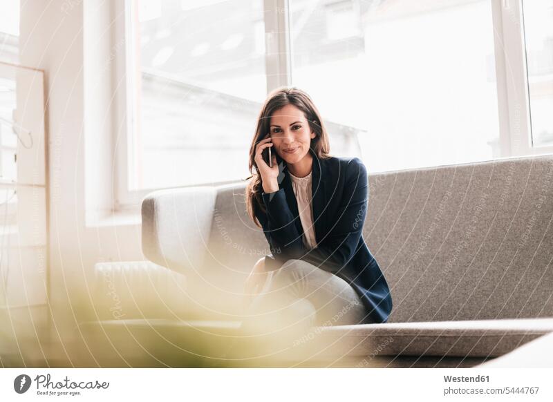 Portrait of smiling businesswoman with cell phone on couch businesswomen business woman business women attractive beautiful pretty good-looking Attractiveness