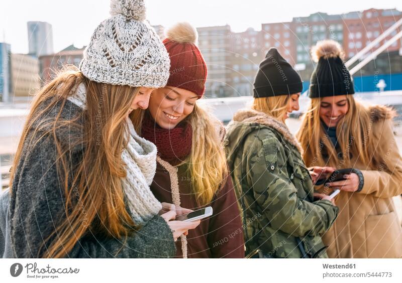 Four friends with their smartphone mate female friend caps hat hats telecommunication phones telephone telephones cell phone cell phones Cellphone mobile