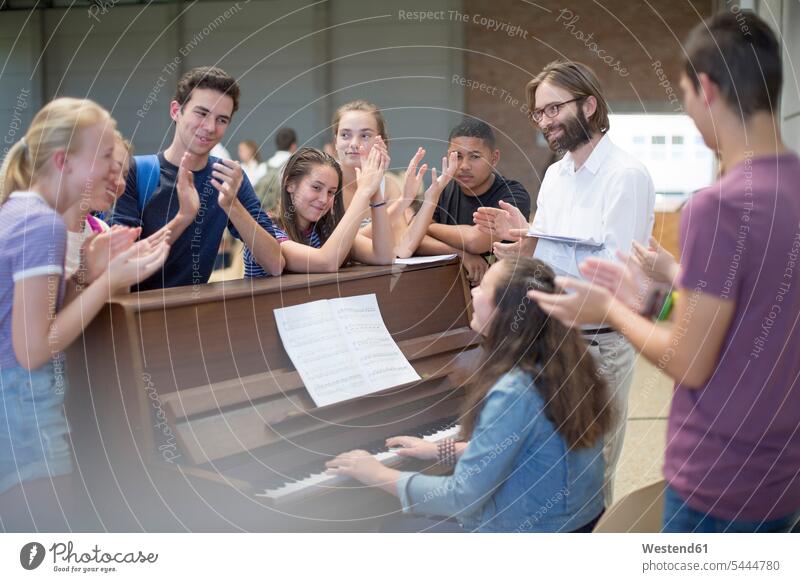 Teacher with group of students standing around piano and applauding pianos teacher instructor teachers pupils clapping hands applause Clapping clap hands