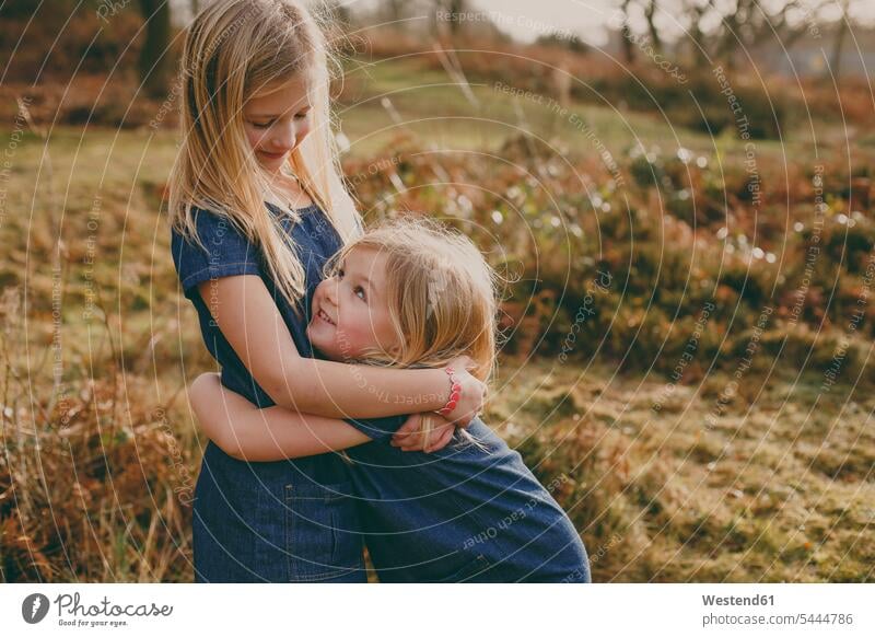 Two cute blond sisters cuddling outdoors girl females girls embracing embrace Embracement hug hugging smiling smile child children kid kids people persons
