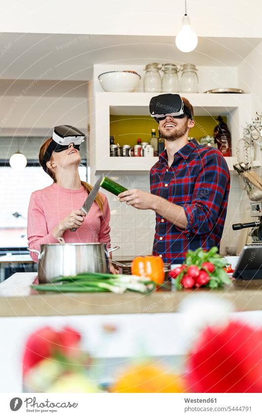 Happy young couple wearing VR glasses cooking together in kitchen virtual reality twosomes partnership couples specs Eye Glasses spectacles Eyeglasses happiness