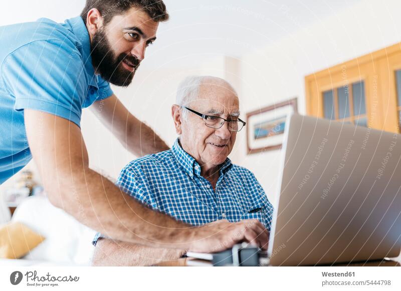 Adult grandson teaching his grandfather to use laptop grandsons grandpas granddads grandfathers Laptop Computers laptops notebook senior men senior man