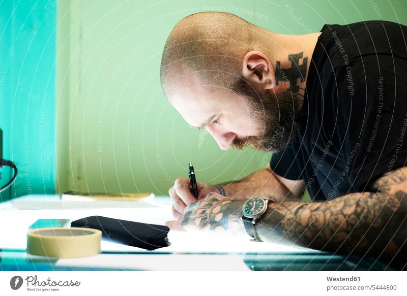 Tattoo artist designing motif on light table in studio tattoo tattoos sketch drawing sketching tattooist tattooer man men males tattooed body art Body Adornment