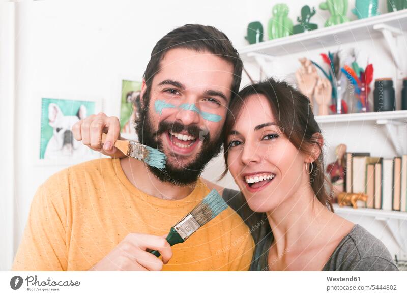 Portrait of happy young couple holding paintbrushes painting twosomes partnership couples laughing Laughter happiness people persons human being humans