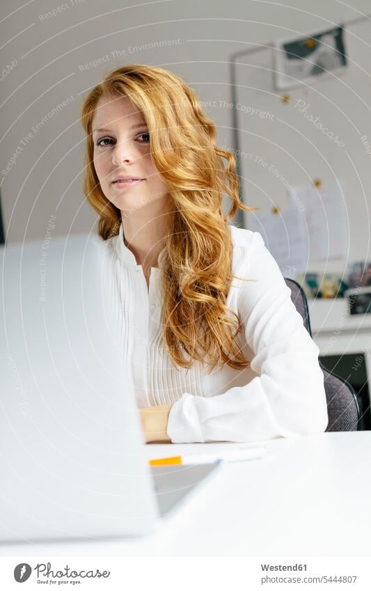 Portrait of smiling young woman with laptop at desk in office smile businesswoman businesswomen business woman business women offices office room office rooms