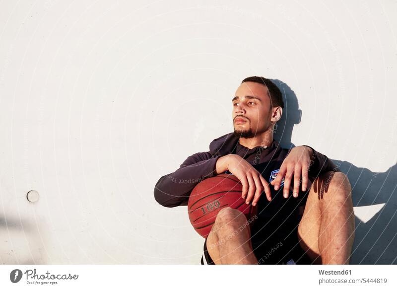 Young man with basketball having a break resting basketballs men males sitting Seated exercising exercise training practising Basketball sport sports Adults