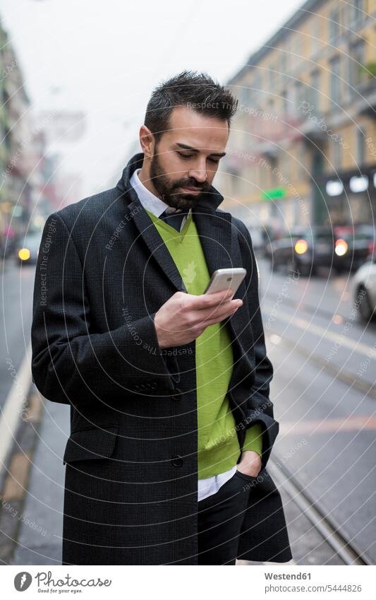 Businessman in the city checking cell phone Business man Businessmen Business men town cities towns standing mobile phone mobiles mobile phones Cellphone