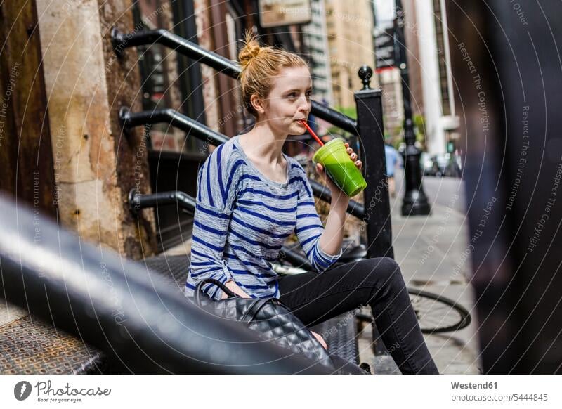 USA, New York City, woman sitting on stoop drinking a smoothie in Manhattan females women Seated Smoothies Adults grown-ups grownups adult people persons