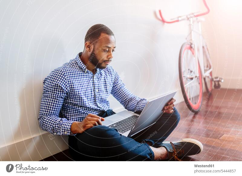 Man using laptop sitting on wooden floor with bicycle in background Businessman Business man Businessmen Business men Laptop Computers laptops notebook Seated