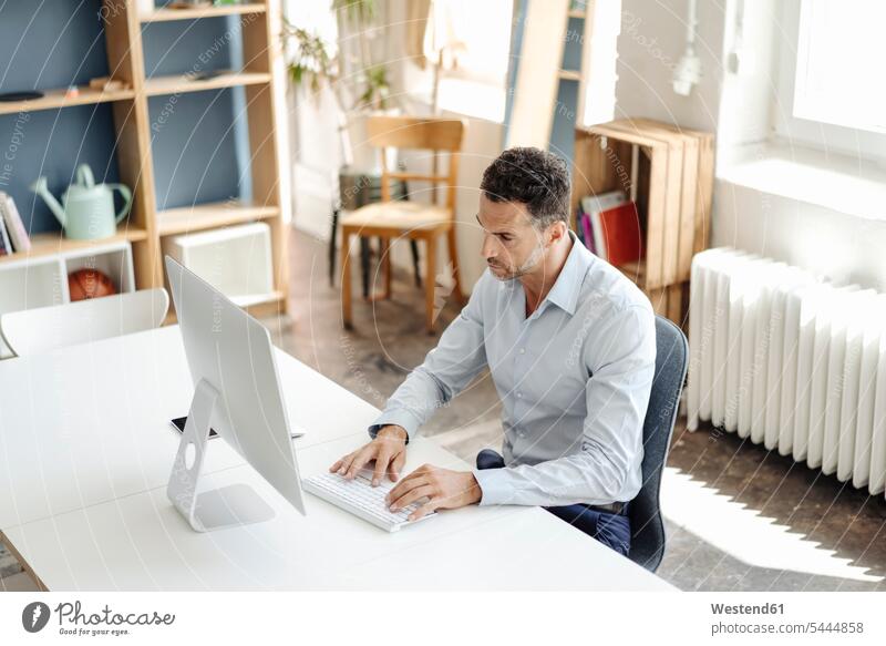 Businessman using computer at desk in office computers offices office room office rooms Business man Businessmen Business men workplace work place place of work