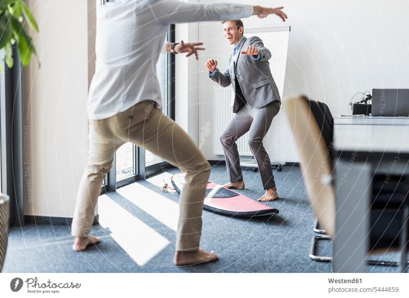 Two playful colleagues with surfboard in office Fun having fun funny offices office room office rooms surfboards laughing Laughter Businessman Business man