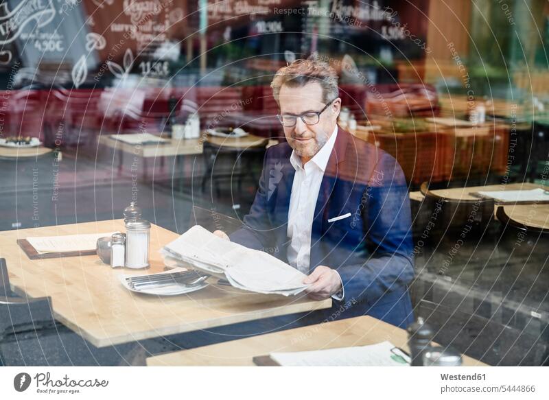 Mature businessman in cafe reading newspaper newspapers Businessman Business man Businessmen Business men business people businesspeople business world