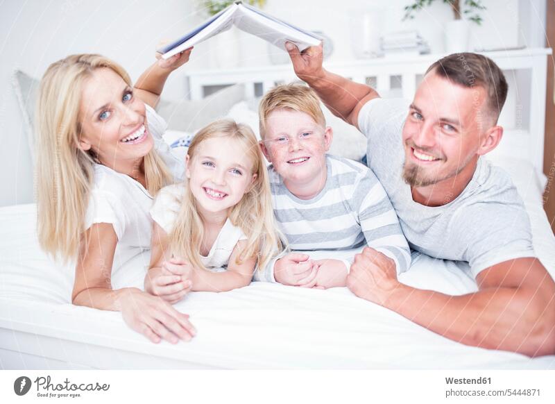 Portrait of smiling parents holding book over children in bed lying laying down lie lying down portrait portraits beds relaxed relaxation family families smile