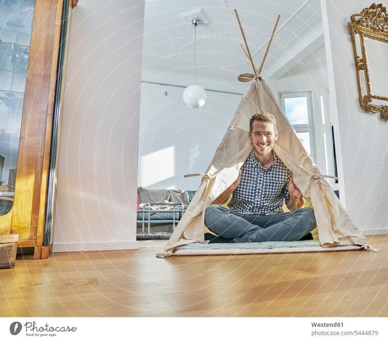 Smiling man sitting on floor in a teepee smiling smile men males tent tents Adults grown-ups grownups adult people persons human being humans human beings