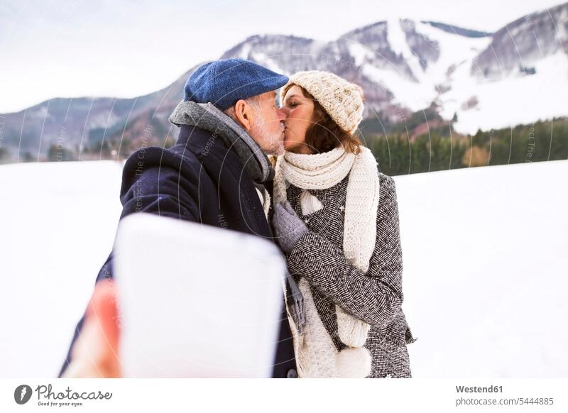Senior couple kissing in winter landscape while taking selfie with cell phone Selfie Selfies kisses senior couple elder couples senior couples adult couple