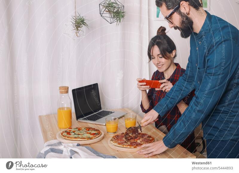 Young couple eating pizza and drinking juice for lunch, woman taking pictures with smart phone photographing laptop Laptop Computers laptops notebook twosomes