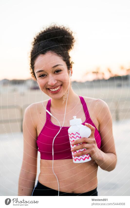 Portrait of smiing young woman with drinking bottle and earphones females women portrait portraits jogger joggers female jogger Adults grown-ups grownups adult