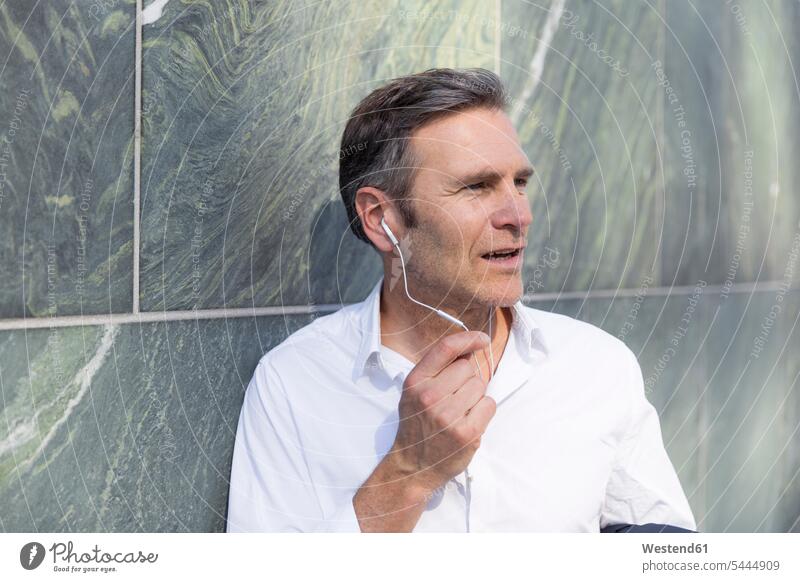 Mature businessman with earphones at a wall Businessman Business man Businessmen Business men ear phone ear phones talking speaking business people