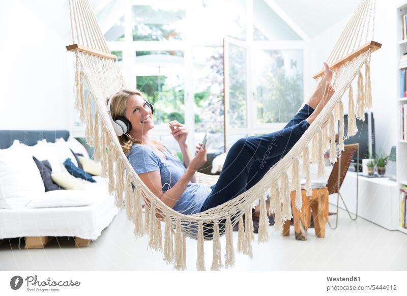 Relaxed woman at home lying in hammock listening to music relaxed relaxation smiling smile headphones headset laying down lie lying down females women hammocks