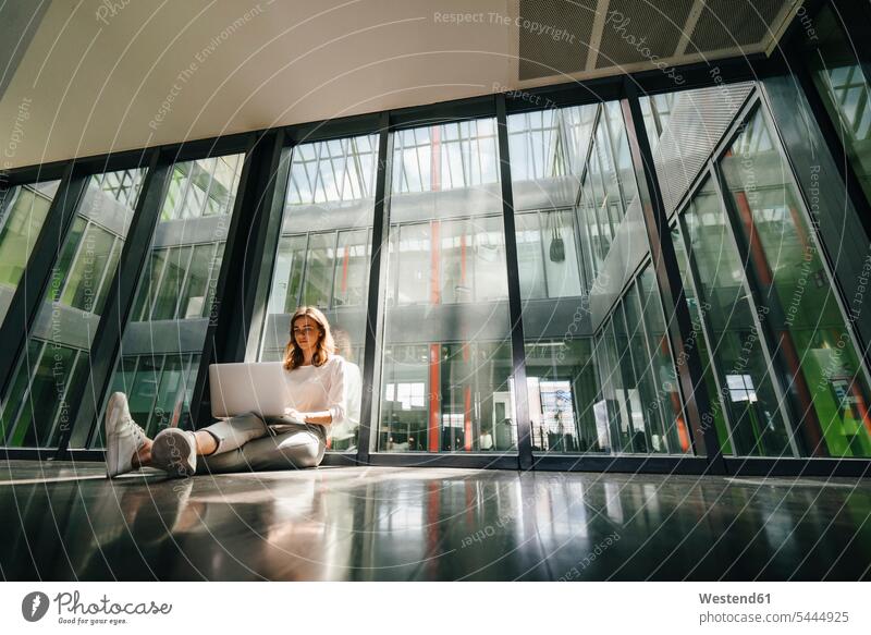 Businesswoman sitting on ground in empty office, using laptop alone solitary solo Seated Sitting On The Floor Sitting On Floor Laptop Computers laptops notebook
