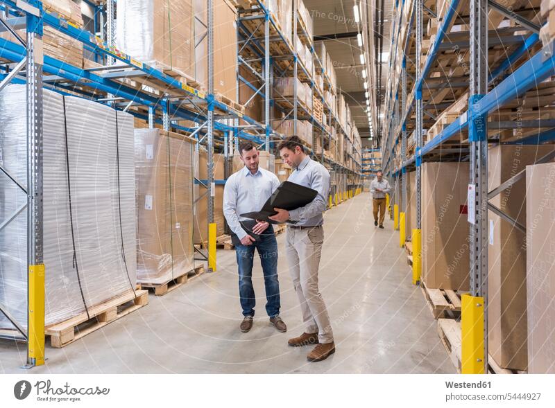 Two men with folder talking in factory warehouse colleagues speaking working At Work man males storehouse storage Adults grown-ups grownups adult people persons