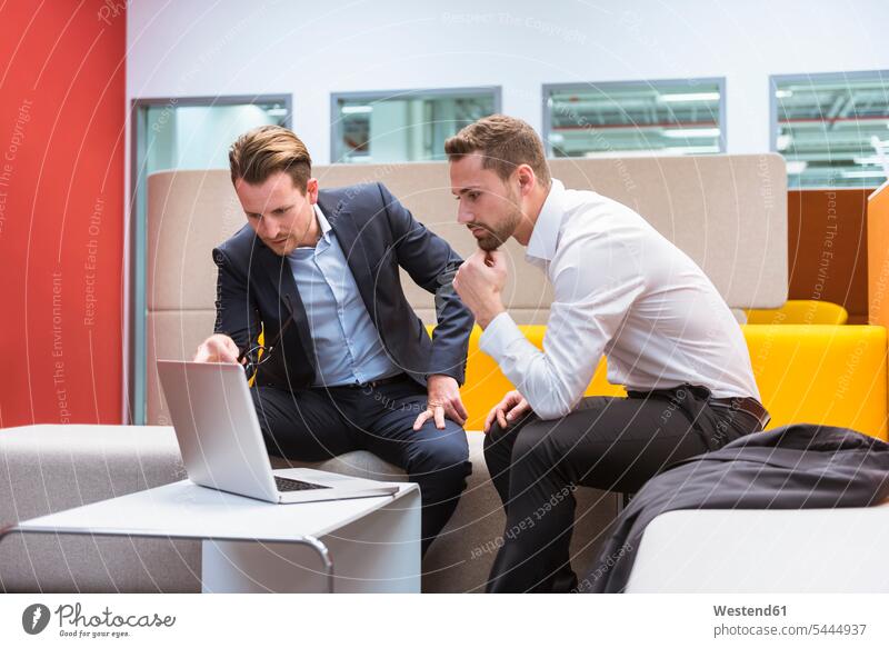 Businessmen sitting in conversation pit, discussing in front of laptop colleagues Seated using laptop using a laptop Using Laptops discussion work meeting