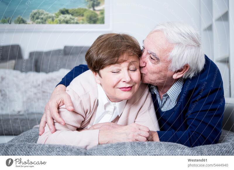 Senior couple lying on couch, hugging and kissing kisses embracing embrace Embracement twosomes partnership couples settee sofa sofas couches settees