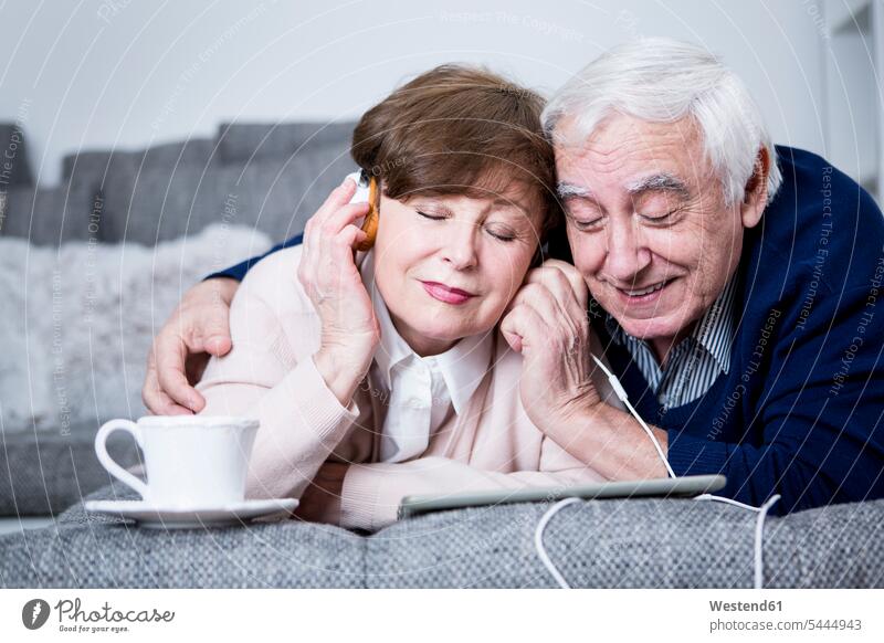Senior couple lying on couch, listening music from digital tablet laying down lie lying down senior adults seniors old digitizer Tablet Computer Tablet PC
