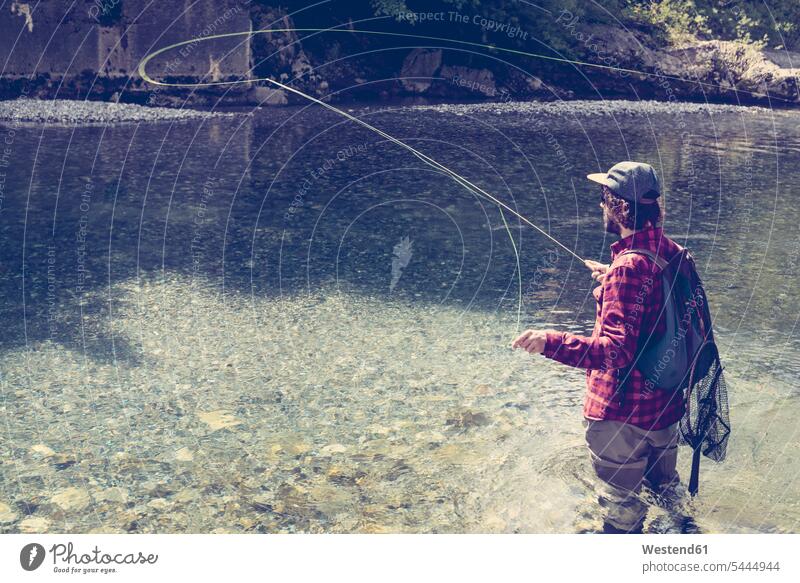 Man with backpack casting fly fishing pole at river - Stock Image