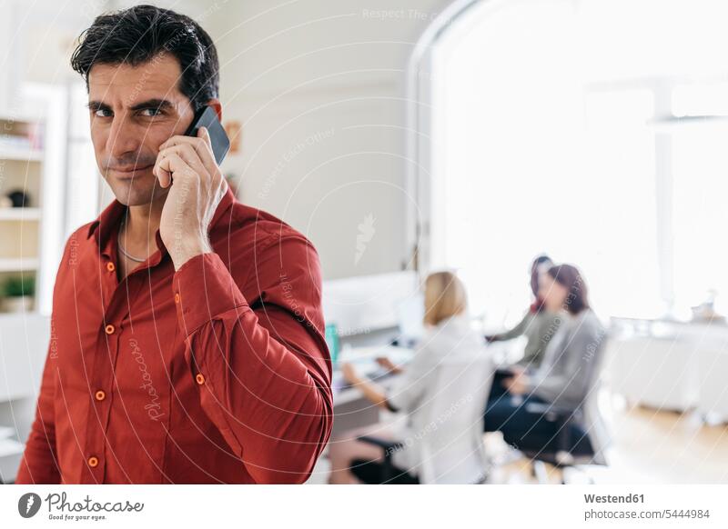 Businessman talking on the phone in office with colleagues working in background Small Business self-employment self-employed accessibility accessible