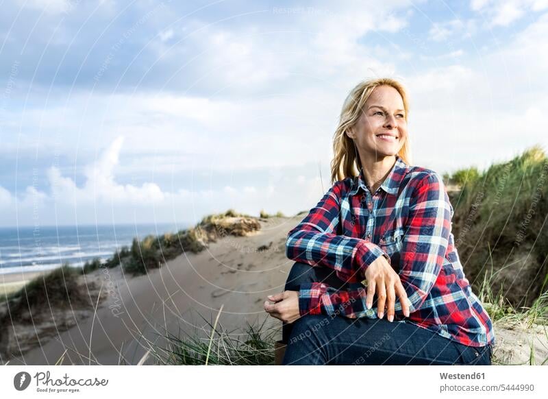 Smiling woman sitting in dunes Seated smiling smile sand dune sand dunes females women beach beaches Adults grown-ups grownups adult people persons human being