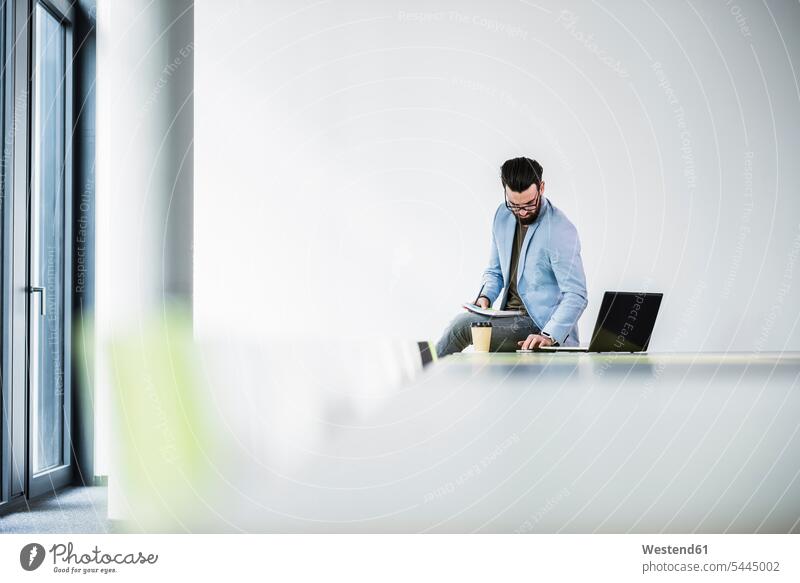 Young businessman sitting on desk, working desks laptop Laptop Computers laptops notebook At Work Businessman Business man Businessmen Business men office