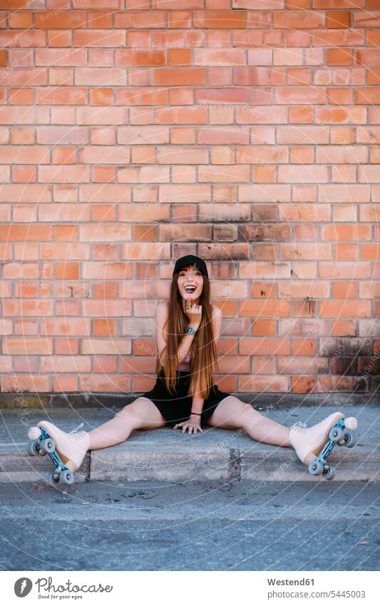 Portrait of laughing young woman with roller skates sitting on sidewalk females women Roller-Skate Adults grown-ups grownups adult people persons human being