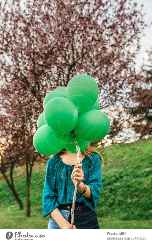 Young woman hiding behind green balloons females women Adults grown-ups grownups adult people persons human being humans human beings hide standing colour