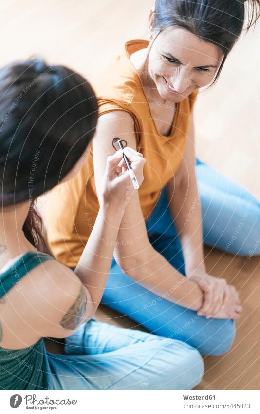Woman painting tattoo on arm of another woman smiling smile females women tattoos Adults grown-ups grownups adult people persons human being humans human beings