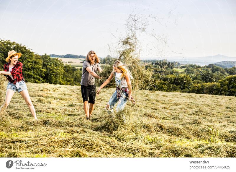 Carefree friends playing with hay in a field Fun having fun funny relaxed relaxation Field Fields farmland rural country countryside Hay throwing mate relaxing