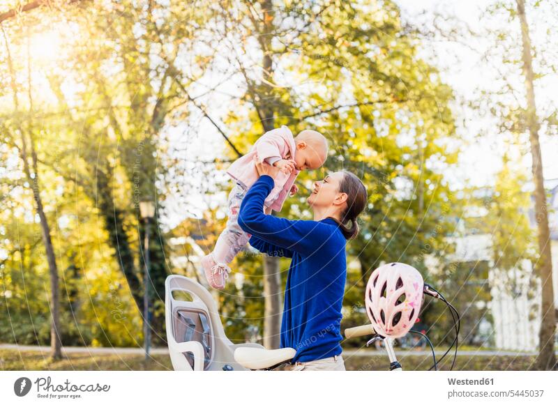 Mother and daughter riding bicycle, lifting baby from children's seat bikes bicycles mother mommy mothers ma mummy mama cycling helmet Bike Helmet