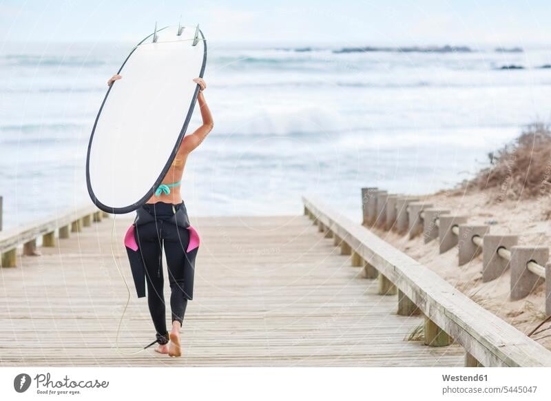 Woman walking to beach with surfboard woman females women carrying surfing surf ride surf riding Surfboarding beaches surfboards going Adults grown-ups grownups