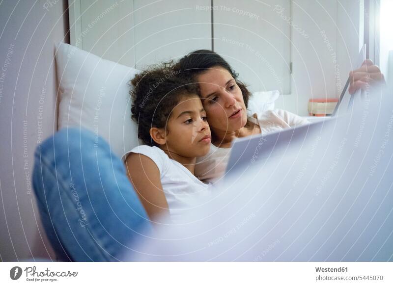 Mother and daughter lying in bed, reading children's book beds mother mommy mothers ma mummy mama books reading out read out laying down lie lying down