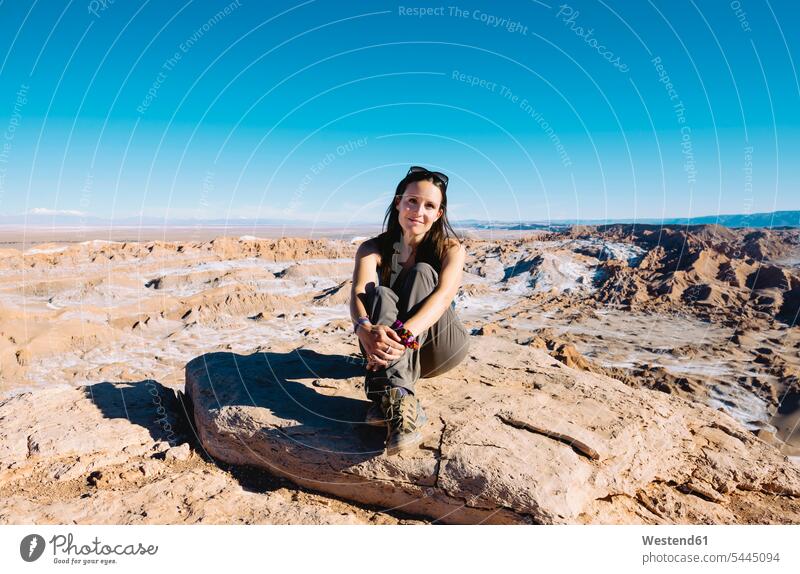 Chile, Atacama Desert, smiling woman sitting on a rock at sunlight females women Adults grown-ups grownups adult people persons human being humans human beings
