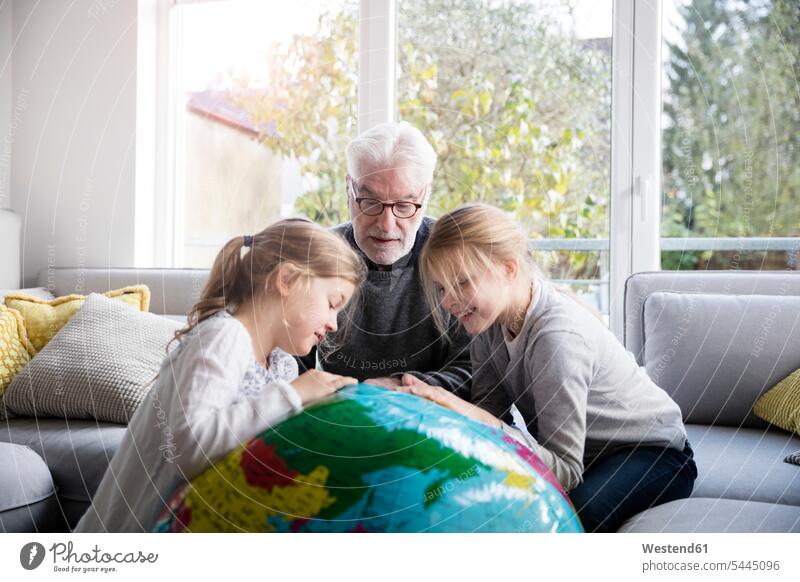 Two girls and grandfather with globe in living room females living rooms livingroom grandpas granddads grandfathers globes child children kid kids people