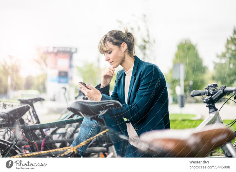 Businesswoman using cell phone outdoors surrounded by bicycles businesswoman businesswomen business woman business women females bikes mobile phone mobiles