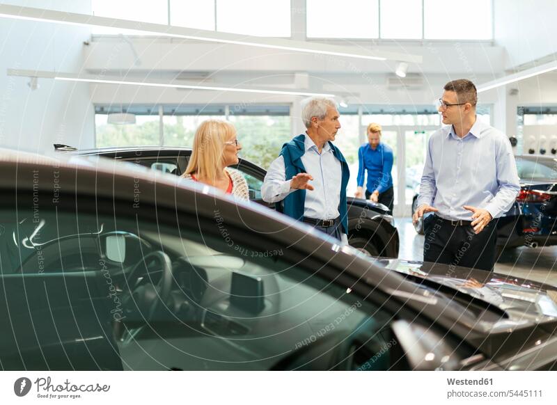 Salesman advising customers in car dealership female customer choosing select choose selecting selling automobile Auto cars motorcars Automobiles counseling