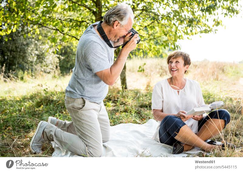 Happy senior man taking picture of his wife in meadow meadows smiling smile camera cameras photographing couple twosomes partnership couples people persons