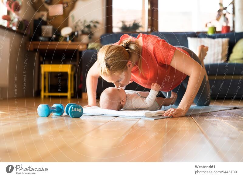 Happy mother kissing baby at home lying on mat next to dumbbells mommy mothers mummy mama kisses infants nurselings babies exercising exercise training