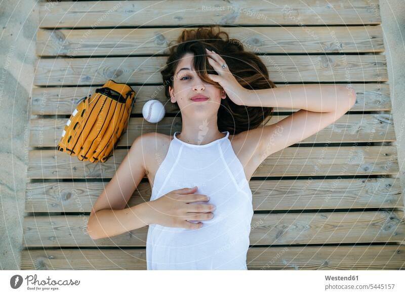 Young woman lying on wooden path next to ball and baseball glove females women laying down lie lying down Adults grown-ups grownups adult people persons