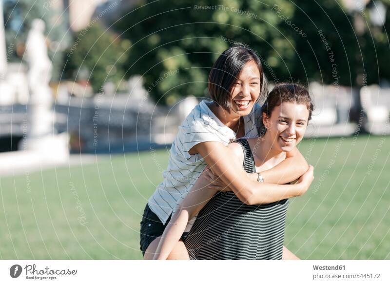Young woman giving her friend a piggyback ride in the park female friends piggy-back pickaback Piggybacking Piggy Back portrait portraits mate friendship